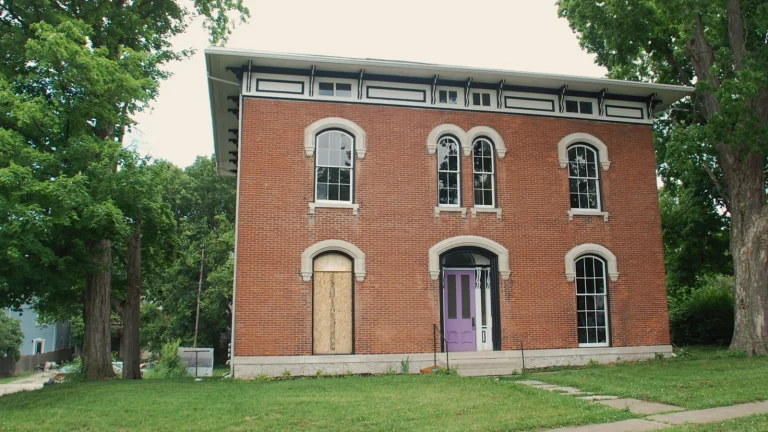 Empty two-story red brick house with boarded windows, a vacant building that may need city registration
